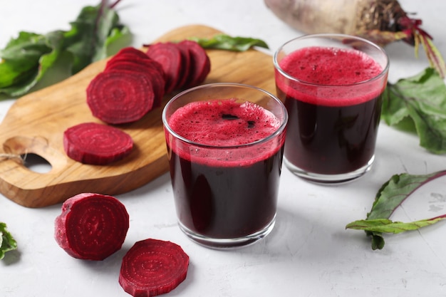 Zwei Glas frischer Rote-Bete-Saft und gehackte Rübe auf Holzbrett auf grauem Hintergrund. Nahansicht