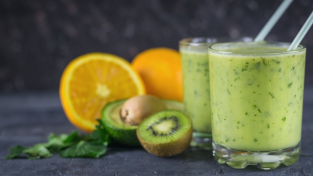 Zwei Glas Glas gefüllt mit dem Smoothie der Avocado auf einem schwarzen Holztisch mit Früchten. Diät vegetarisches Essen.