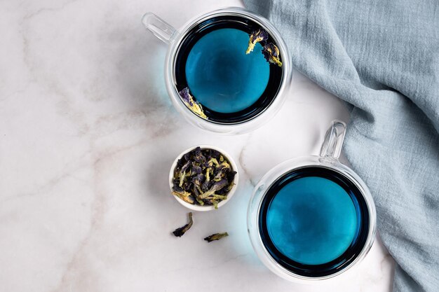 Zwei Glastassen mit blauem Anchan-Tee aus Schmetterlingserbsenblume auf Marmorhintergrund, Draufsicht.