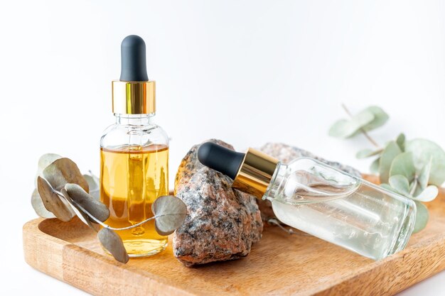 Foto zwei glaströpfchenflaschen mit einer pipette mit schwarzer und goldener gummistiefel auf holzplatte mit stein und verschwommenem eukalyptus natur hautkonzept organische spa-kosmetik trendy-konzept