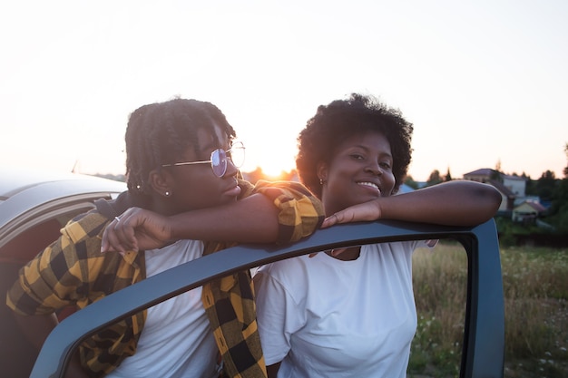 Zwei glückliche afroamerikanische Frauen nahe dem Auto bei Sonnenuntergang, Lebensstil.