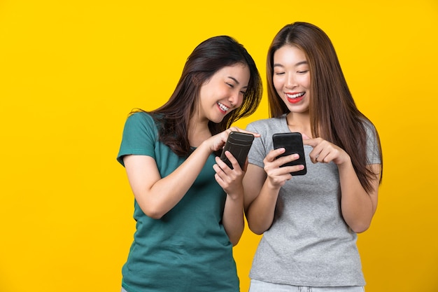 Zwei glückliche asiatische lächelnde junge Spielerin, die intelligentes Mobiltelefon verwendet und Spiele spielt