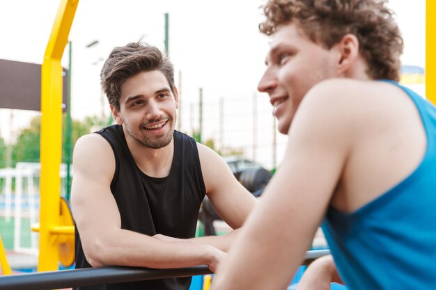 Zwei glückliche Fitness-Männer trainieren draußen auf dem Spielplatz und unterhalten sich