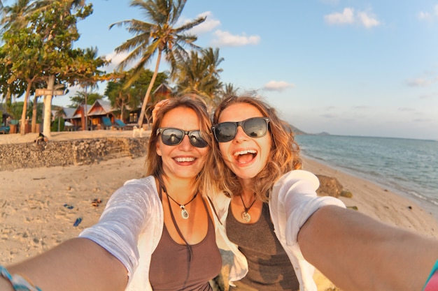 Zwei glückliche Freundinnen, die selfie auf der Küste von tropischem Meer machen