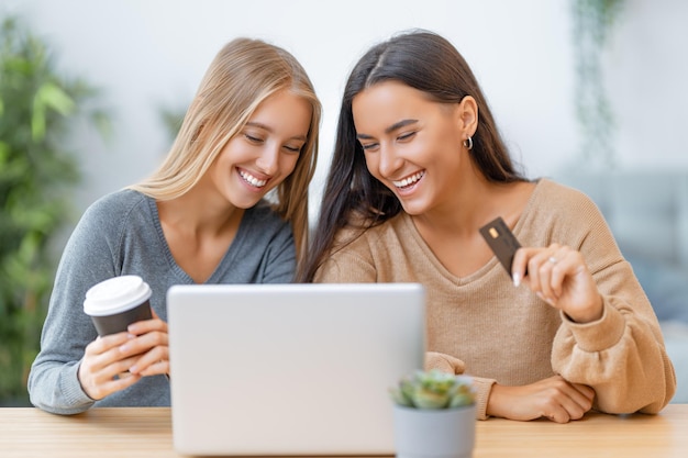 Zwei glückliche junge Frauen, die Online-Einkäufe tätigen. Mädchen, die zu Hause einkaufen.