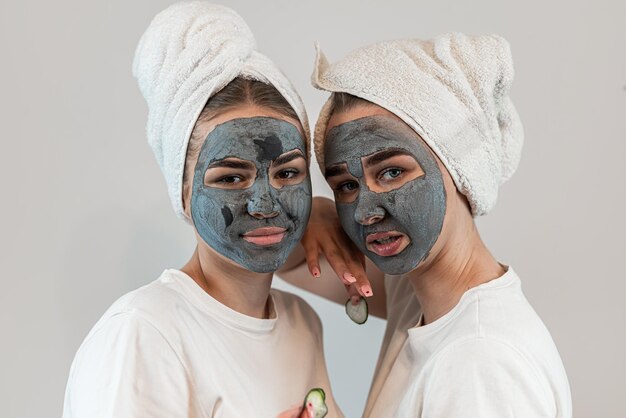 Zwei glückliche junge Frauen tragen eine Tonmaske auf ihr Gesicht auf und genießen ihre Freizeit