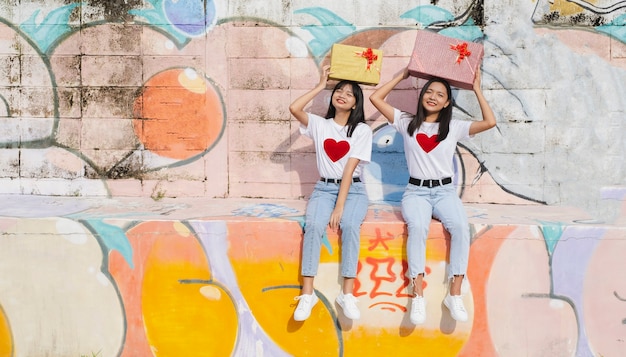 Zwei glückliche junge Mädchen mit Geschenkbox auf buntem Hintergrund. Asiatisches Mädchen.