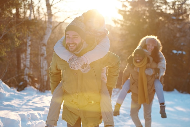 Zwei glückliche junge Paare in Winterkleidung, die sich an einem sonnigen Tag amüsieren