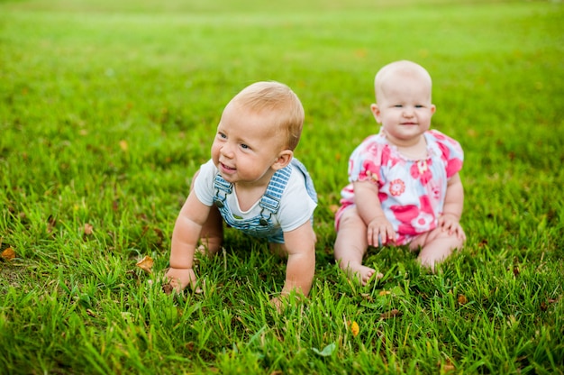 Zwei glückliche Jungen und ein Mädchen im Alter von 9 Monaten sitzen im Gras und interagieren, reden, schauen sich an.