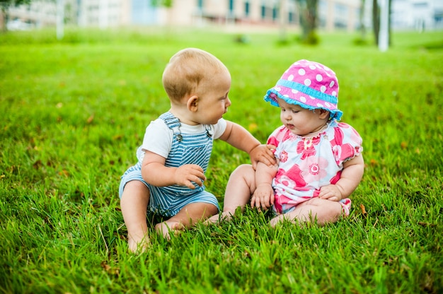 Zwei glückliche Jungen und ein Mädchen im Alter von 9 Monaten sitzen im Gras und interagieren, reden, schauen sich an.