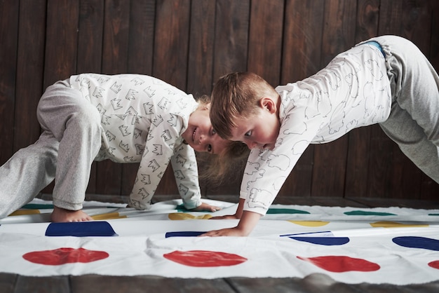 Zwei glückliche Kinder, die am Twister im Haus spielen. Bruder und Schwester haben eine lustige Zeit im Urlaub