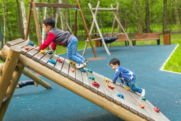 Zwei glückliche kleine asiatische Jungs spielen im Sommer im Freien auf dem Holzspielplatz