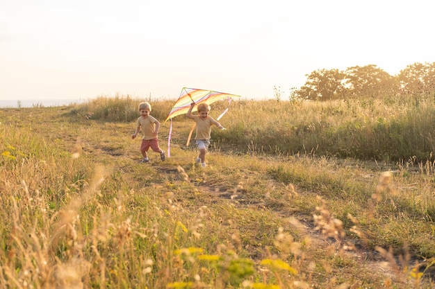 zwei glückliche kleine kinder, die sich bei sonnenuntergang mit drachen in der natur amüsieren