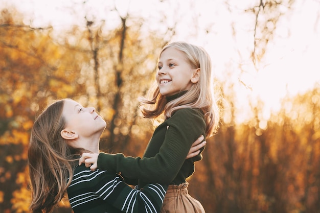 Zwei glückliche kleine Schwestern lachen, haben Spaß und spielen im Herbst in der Natur im Freien