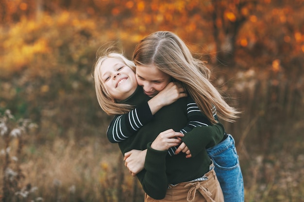 Zwei glückliche kleine Schwestern lachen, haben Spaß und spielen im Herbst in der Natur im Freien