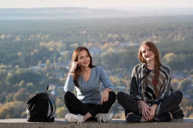 Zwei glückliche Mädchen, die auf a der Natur sitzen. Bleiben Sie mit einem Freund, Ferien Urlaub