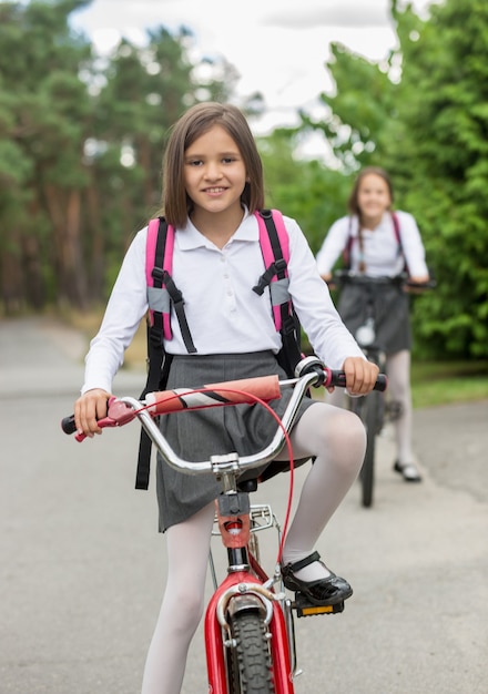 Zwei glückliche Mädchen in Schuluniform, die morgens auf Fahrrädern fahren