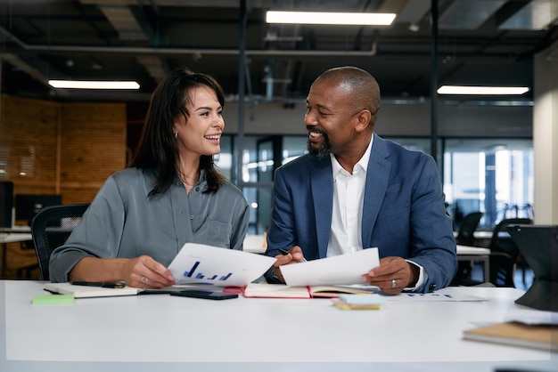 Zwei glückliche Multiracial-Kollegen lächelnd mit Grafik-Dokumenten im Büro.
