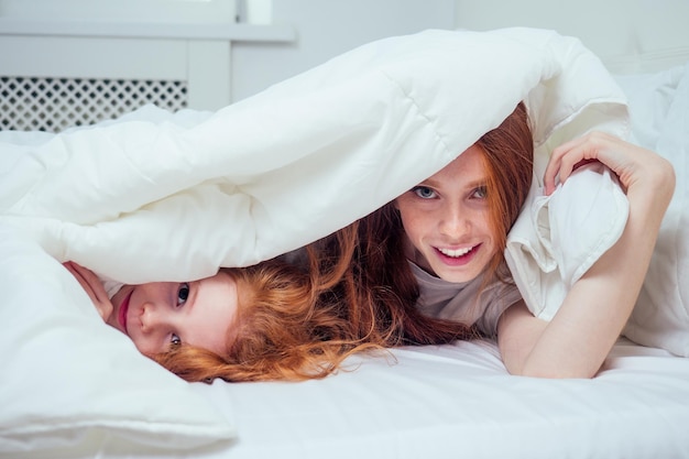 Foto zwei glückliche redhaired ingwermädchen, die verstecken spielen und unter weißer decke suchen. konzept für den ausbruch des corona-virus in selbstisolation.