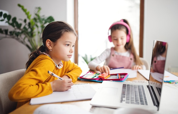 Zwei glückliche Schulmädchenschwestern mit Laptop zu Hause, Fernunterricht.