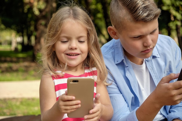 Zwei glückliche Teenager-Freunde, die ein Handy benutzen, während sie sich im Park entspannen Probleme des modernen sozialen Netzwerklebens von Jugendlichen online