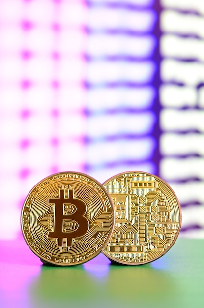 Zwei goldene Bitcoins liegen auf der grünen Fläche vor dem Hintergrund der Anzeige