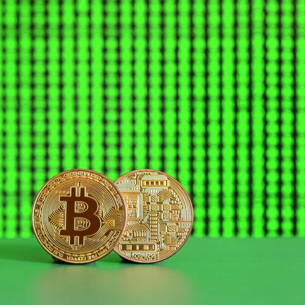 Zwei goldene Bitcoins liegen auf der grünen Fläche vor dem Hintergrund der Anzeige