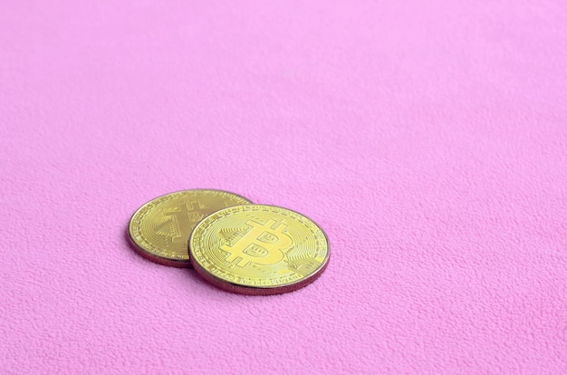 Zwei goldene Bitcoins liegen auf einer Decke aus weichem und flauschigem hellrosa Fleece