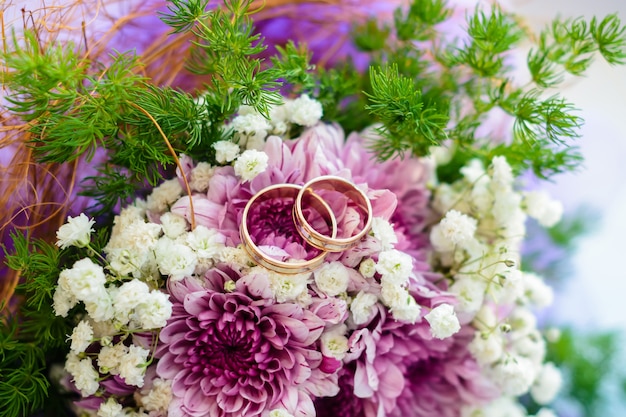 Zwei goldene Eheringe liegen auf den Blumen eines Blumenstraußabschlusses oben