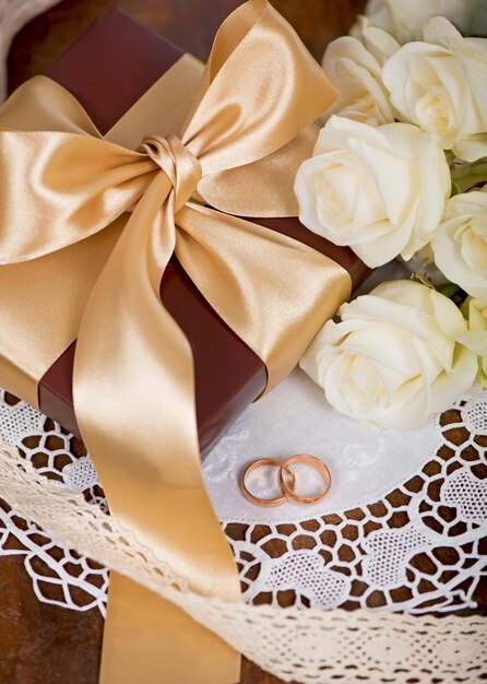Zwei goldene Eheringe und ein Blumenstrauß aus weißer Rose mit grünen Blättern auf Holz