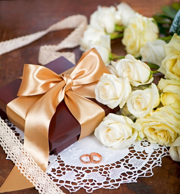 Zwei goldene Eheringe und ein Blumenstrauß aus weißer Rose mit grünen Blättern auf Holz