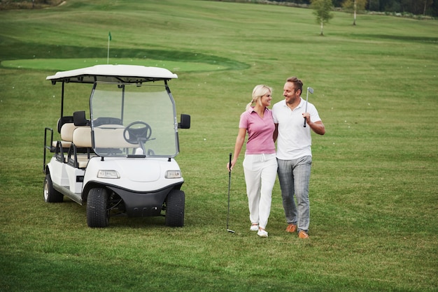 Zwei Golfer, eine Frau und ein Mann, gehen gemeinsam zum nächsten Loch. Eine Studentin geht mit ihrem Personal Trainer und freut sich über ihren sportlichen Erfolg