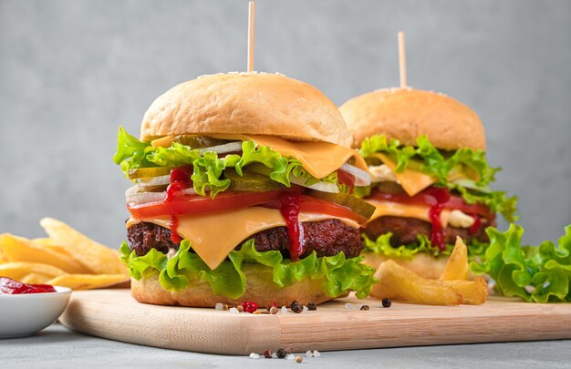 Zwei große, leckere Burger und Pommes Frites an einer grauen Wand. Seitenansicht, Nahaufnahme.