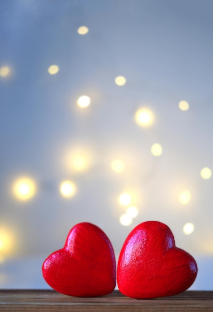 Zwei große rote Herzen liegen auf einem Holztisch auf einem unscharfen Hintergrund mit einer Seite der Girlande, einem vertikalen Bild mit weichem Fokus und einem Platz für Text