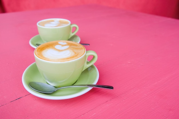 Zwei grüne Tassen Cappuccino mit Latte Art auf rosa Pastellhintergrund