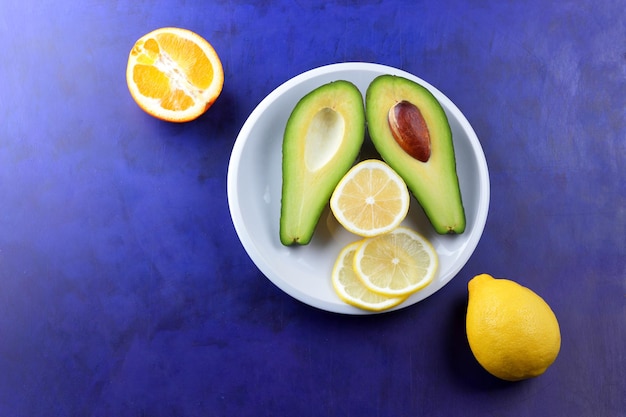 Zwei Hälften einer reifen Avocado mit Samen auf einem weißen Teller Closeup grüne gesunde Frucht mit Zitrusfrüchten auf blauem Hintergrund