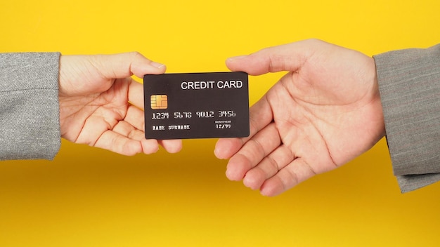 Zwei Hände senden und halten eine schwarze Kreditkarte auf gelbem Hintergrund Arme tragen einen grauen Anzugx9