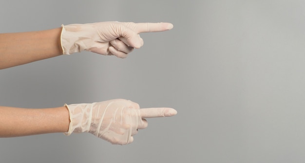 Zwei Hände zeigen und tragen medizinische Handschuhe auf grauem Hintergrund.