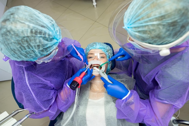 Zwei Helfer in Spezialkleidung, Masken, Mützen, Handschuhen helfen bei der Durchführung der Operation zum Zahnarzt