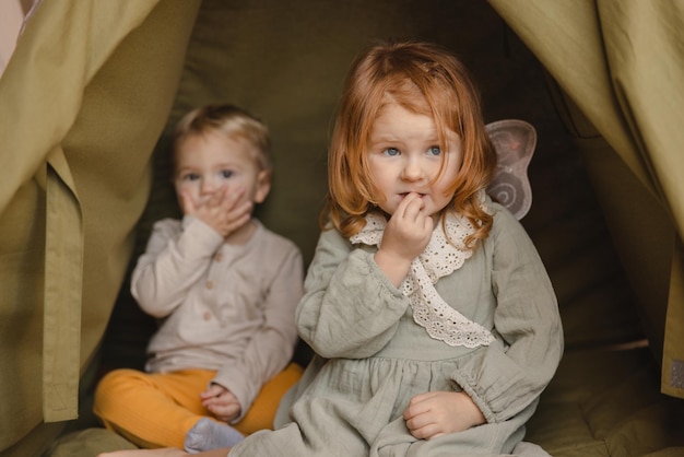 Zwei hellhäutige kleine Kinder im Alter von 23 Jahren, Junge und Mädchen in Freizeitkleidung, schauen weg, wenn sie drinnen sitzen Bruder- und Schwesterkonzept
