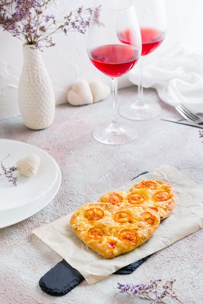 Zwei herzförmige Pizzen auf Papier und zwei Gläser Wein auf einem gedeckten Tisch zum Valentinstag. Vertikale Ansicht