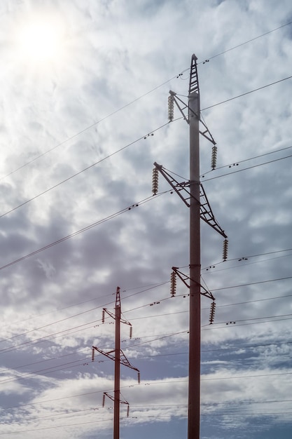 Zwei Hochspannungsmasten mit Betonsockel vor bewölktem Himmel