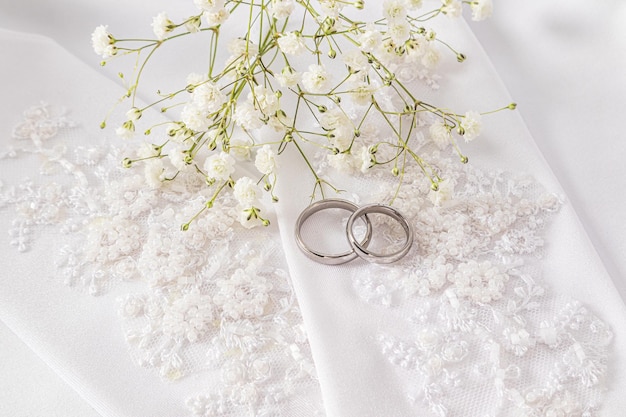 Zwei Hochzeitsringe aus weißem Gold liegen auf den schicken Hochzeitshandschuhen der Braut. Weißer Satin-Hintergrund