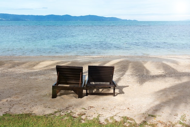 Zwei hölzerne Sonnenliegen am tropischen Strand gegen Seelandschaft.