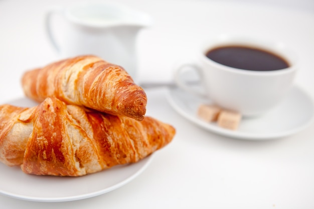 Zwei Hörnchen und eine Tasse Kaffee auf weißen Platten mit Zucker und Milch