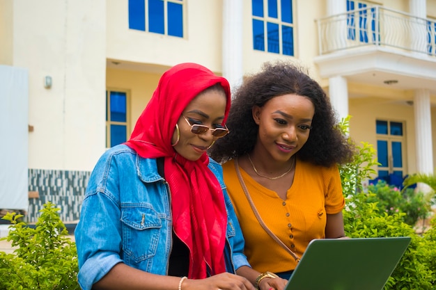 Zwei hübsche afrikanische Damen, die den Laptop bedienen.