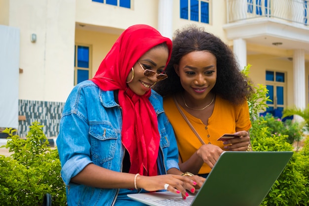 Zwei hübsche afrikanische Damen, die ihre Kreditkarte und ihren Laptop benutzen, um online einzukaufen.