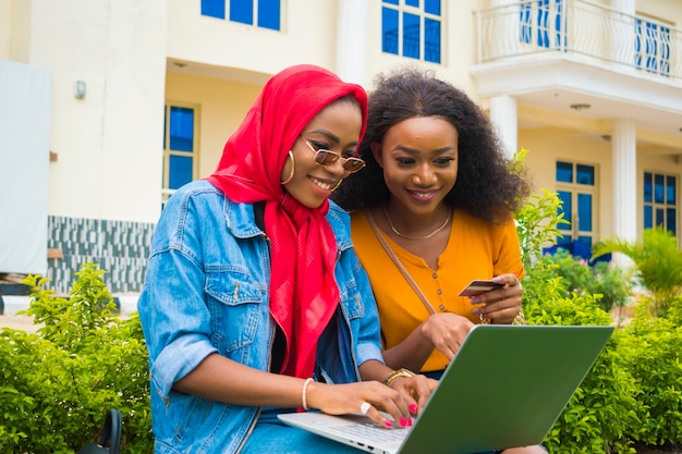 Zwei hübsche afrikanische Damen, die ihre Kreditkarte und ihren Laptop benutzen, um online einzukaufen.