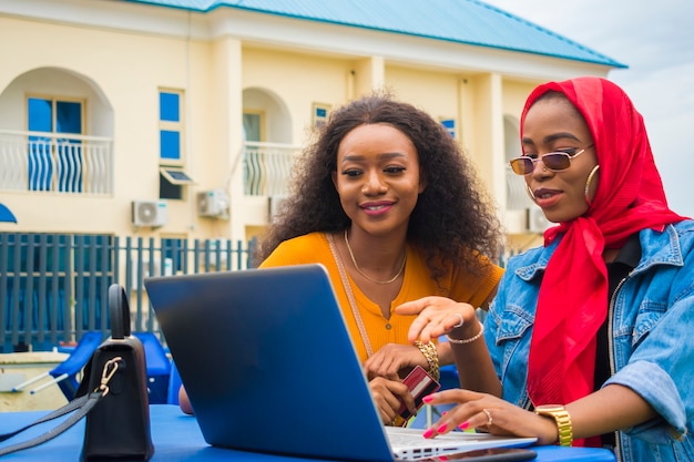 Zwei hübsche afrikanische Damen, die ihre Kreditkarte und ihren Laptop benutzen, um online einzukaufen.