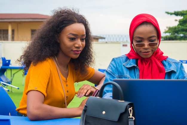 Zwei hübsche afrikanische Damen, die ihre Kreditkarte und ihren Laptop benutzen, um online einzukaufen.